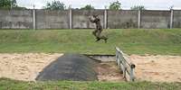 Ein Soldat springt über den Balkengraben auf der Hindernisbahn.