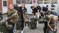 Mehrere junge Frauen packen ihren Rucksack mit militärischer Ausrüstung