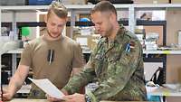 Zwei Soldaten schauen in einem Lagerraum gemeinsam auf ein Blatt Papier. 