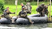 Mehrere Soldaten mit Rettungswesten steigen in ein schwarzes Schlauchboot auf einem Fluss.