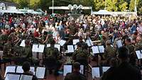 Ein Militärorchester sitzt auf einem Platz und spielt, davor zahlreiche Zuhörer.