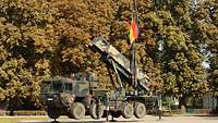 Ein Startgerät des Waffensystems Patriot steht auf dem Antreteplatz und ist mit einer Deutschlandflagge geschmückt. 