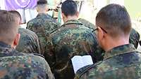 Soldatinnen und Soldaten singen beim Feldgottesdienst aus einem Gesangbuch.