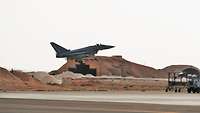 Kampflugzeug landet vor Wüstenpanorama im Hintergrund ein Flugzeugshelter