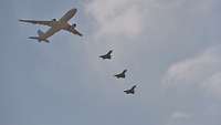 Formation aus Militärtransportflugzeug und drei Kampfflugzeugen im Flug von unten 