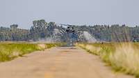 A helicopter flying above a dirt road. On the sides, dust particles fall in an arch.
