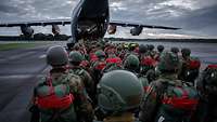 Mehrere Soldaten mit Helmen und Fallschirmen steigen über die Heckklappe in einem Airbus A400M ein