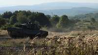 Ein Kampfpanzer Leopard 2 A6 fährt einen Weg entlang, im Hintergrund Wälder.