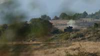Ein Panzer Leopard steht auf einer leichten Erhöhung, verdeckt durch eine kleine Baumreihe an seiner linken Seite.