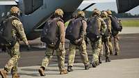 Mehrere Soldaten tragen auf ihren Rücken einen Fallschirmrucksack und steigen in ein Flugzeug ein
