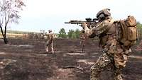 Drei Soldaten mit Waffe im Anschlag auf verbrannter Heide