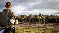 Soldaten stehen angetreten in Formationen. Ein Soldat steht vor ihnen und spricht zu ihnen.