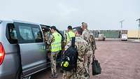 Vier Soldaten steigen in einen grauen Kleinbus. Im Hintergrund erkennt man Container im Camp Sonic.