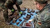 Zwei Soldaten mit Tablett dokumentieren die gefundene Munition.