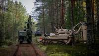 Drei spezielle militärische Räumfahrzeuge hintereinander auf einem Waldweg.