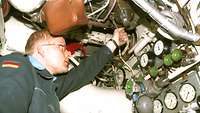 A soldier engages a lever in a confined space with gauges, valves and pipes.