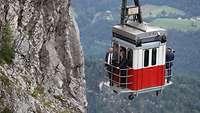 Two men are standing on the platform of a cable car riding up a mountain.