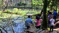 Mehrere Menschen stehen an einem Weiher.