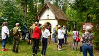 Mehrere Menschen stehen vor einer Kapelle im Wald. 