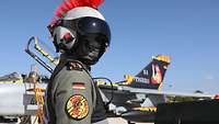 Eine Jetpilot steht mit Schutzhelm und Gesichtstuch im Portrait vor einem Tornado in Sonderfolierung