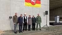 Gruppenbild mit zwei weiblichen und vier männlichen Personen, eine davon in Uniform, vor einem Rohbau