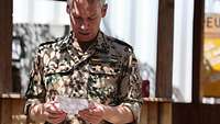 Der Militärpfarrer steht vor einem Tisch und schaut auf seine Notizen, die er in der Hand hält.