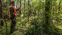 Ein Soldat steht im Wald und zeigt mit einem orangefarbenen Pfeil auf einen getarnten Soldaten. 