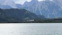 Der Forggensee mit Blick auf Füssen, umgeben von Bergen und Wäldern.