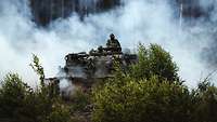 Ein Panzer befindet sich in einem Wald voller Qualm, während zwei Soldaten aus dem Ausguck schauen. 