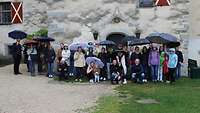 Ein Gruppe Gäste steht für ein Gruppenbild vor einer Burgmauer