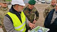 Drei Soldaten und ein Mann in Zivil mit Helm und Warnweste schauen auf ausgedruckte Baupläne