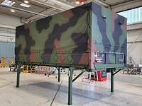 Curtain-sided swap body with camouflage paint on green stilts.