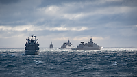 Drei Fregatten und ein Versorgungsschiff fahren bei rauer See in Formation.