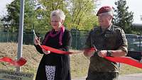 Eine Frau und ein Soldat schneiden ein rotes Band mit jeweils einer Schere durch 