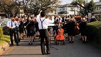 max. 125 Zeichen  Ein japanisches Schulorchester musiziert im Freien auf einer Straße.