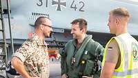 Zwei Soldaten und ein Pilot im Flugdienstanzug stehen vor einem Eurofighter und sprechen miteinander.