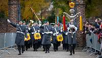 Soldaten in Uniform und mit Instrumenten laufen in mehreren Reihen durch ein Backsteintor.