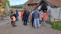 Eine Personengruppe steht vor einem Dorfbackhaus.