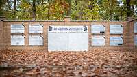 Gedenkstein mit Text "Den Toten zu Ehren" vor einer Mauer mit Gedenktafeln im Wald der Erinnerung