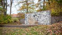 Ein Gedenkstein mit Gravur vor einer Mauer im Wald der Erinnerung