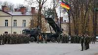 Vor einem Haus und Fahrzeug mit einer deutschen Flagge sind Soldatinnen und Soldaten angetreten.