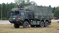 A truck with camouflage paint is standing on a meadow