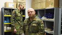 Drei Bundeswehrsoldaten sind in einem Raum vor Regalen mit verschiedenen Materialien.
