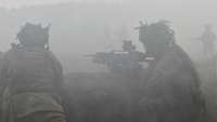 Zwei Soldaten stehen bei weißem Nebel mit Gewehren in einem Graben. Andere stürmen nach vorn.