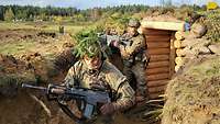 Zwei Soldaten kämpfen sich mit dem Gewehr bei Sonne durch den Schützengraben auf einem Feld. 