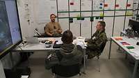 Drei Soldaten in einer Besprechung mit Plänen an den Wänden
