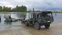 Ein LKW steht am Ufer und lässt ein Teil einer Faltschwimmbrücke ins Wasser.