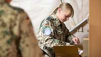 Eine Soldatin packt einen Karton mit medizinischen Produkten