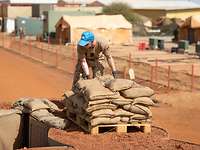 Ein Soldat mit blauem Basecap stapelt Sandsäcke im Camp Castor in Mali