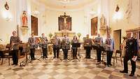 Neun Musiker des Heeresmusikkorps und ein deutscher Oberst im Dienstanzug stehen im vorderen Teil einer Kirche.